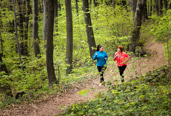 Obraz premium Mother and daughter wearing sportswear and running in forest