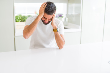 Handsome hispanic man casual white t-shirt at home suffering from headache desperate and stressed because pain and migraine. Hands on head.