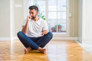 Handsome hispanic man wearing casual t-shirt sitting on the floor at home looking stressed and nervous with hands on mouth biting nails. Anxiety problem.
