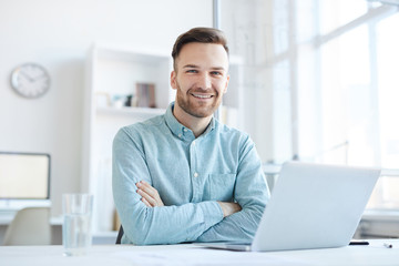 Portrait of handsome entrepreneur smiling happily at camera while posing at workplace in office,...