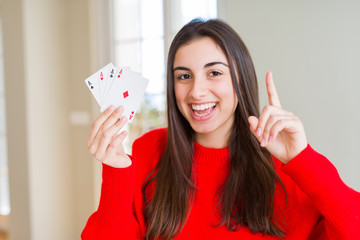 Beautiful young woman gambling playing poker surprised with an idea or question pointing finger with happy face, number one