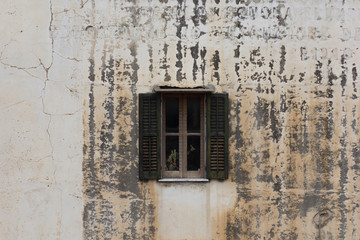 One small window with wooden shutters on aged and cracked wall with invisible inscription
