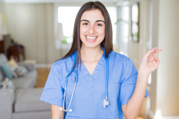 Beautiful young nurse woman wearing uniform and stethoscope at the clinic with a big smile on face, pointing with hand and finger to the side looking at the camera.