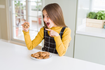 Beautiful young girl kid eating chocolate chips cookies very happy pointing with hand and finger