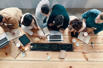 Teamwork. Top view of young modern people in smart casual wear using modern technologies while...