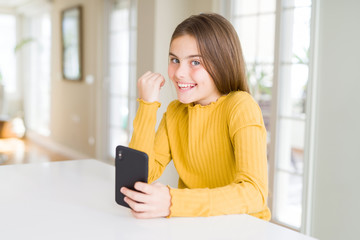 Beautiful young girl kid sending a message using smartphone pointing and showing with thumb up to the side with happy face smiling