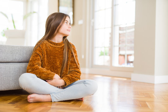 Beautiful Young Girl Kid Sitting On The Floor At Home Looking To Side, Relax Profile Pose With Natural Face With Confident Smile.