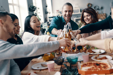 Close friends. Group of young people in casual wear toasting each other and smiling while having a dinner party indoors