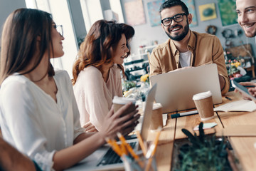 Happy business partners. Group of young modern people in smart casual wear discussing something and smiling while working in the creative office