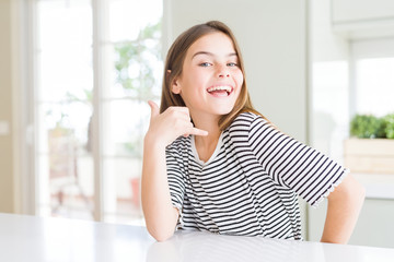 Beautiful young girl kid wearing stripes t-shirt smiling doing phone gesture with hand and fingers like talking on the telephone. Communicating concepts.
