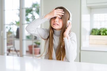 Beautiful young girl wearing headphones listening to music and dancing stressed with hand on head, shocked with shame and surprise face, angry and frustrated. Fear and upset for mistake.