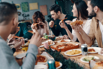 Good food and good friends. Group of young people in casual wear eating pizza and smiling while having a dinner party indoors