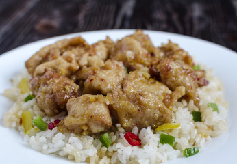 chicken in sweet and sour sauce and rice with vegetables on a white plate on a dark background