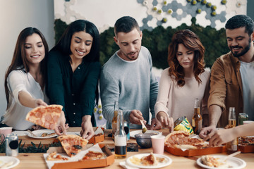 Choosing the best slice. Group of young people in casual wear eating pizza and smiling while having a dinner party indoors
