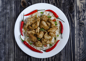 chicken in sweet and sour sauce and rice with vegetables on a white plate on a dark background