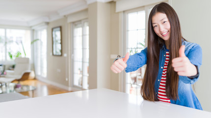Fototapeta na wymiar Young beautiful asian woman with long hair wearing denim jacket approving doing positive gesture with hand, thumbs up smiling and happy for success. Winner gesture.