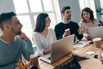 Happy business partners. Group of young modern people in smart casual wear discussing something and smiling while working in the creative office