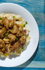 chicken in sweet and sour sauce and rice with vegetables on a white plate blue vertical background