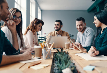 Developing business. Group of young modern people in smart casual wear discussing something and smiling while working in the creative office