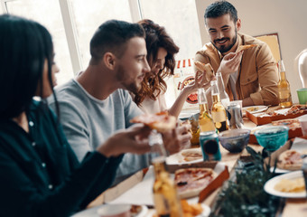 Leave all the worries behind. Group of young people in casual wear eating pizza and smiling while having a dinner party indoors
