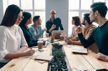 Discussing risky ideas. Group of young modern people in smart casual wear discussing something while working in the creative office