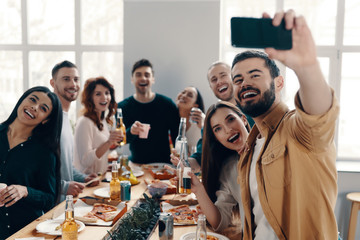 Capturing the moment. Group of young people in casual wear taking selfie and smiling while having a dinner party indoors