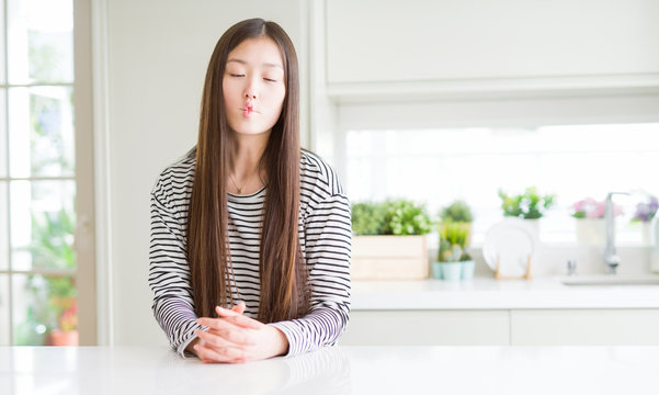 Beautiful Asian woman wearing stripes sweater making fish face with lips, crazy and comical gesture. Funny expression.