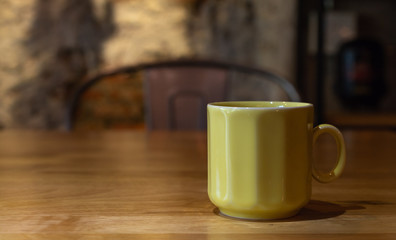 A yellow coffee cup on a wooden table.