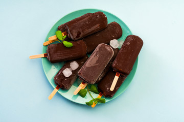 chocolate ice cream popsicle with ice and mint on light blue background