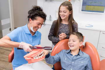 Zahnärztin erklärt spielerisch zwei Kindern, dass richtige Zähneputzen