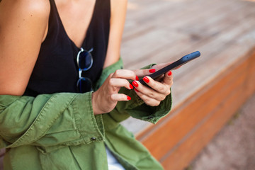 City lifestyle stylish hipster girl using a phone texting on smartphone app in a street.Beautiful young caucasian woman looking at her smartphone and smiling in urban background. 