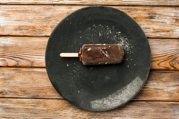 chocolate popsicle ice cream with a stick on a plate, against the background of a wooden table, top view
