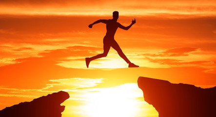 Silhouette of man jump through the gap between hills