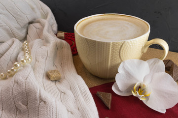 Obraz na płótnie Canvas A Cup of coffee in a cozy style on a cork background and a white knitted blanket. Black and red colors.