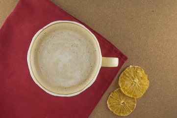 A Cup of coffee in a cozy style on a cork background and a red fabric. Slices of dried orange. Flat...