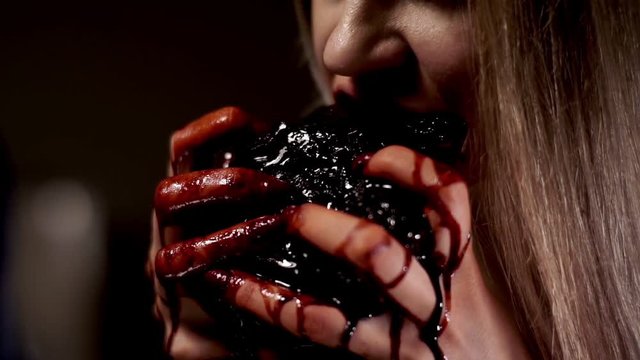 Girl holding bloody hands bleeding heart and eagerly bites off of it pieces