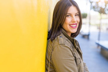 Beautiful young woman smiling confident and cheerful leaning on yellow wall, walking on the street of the city on a sunny day