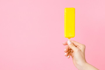 Young woman hand holding bright yellow ice cream with lemon glaze on pastel pink background. Empty place for text, quote or sayings. Front view. 