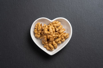A few shelled walnuts lie in a saucer in the shape of a heart on textured slate board