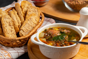 Lentil soup with chicken in a white bowl on a wooden board on a black table and ingredients