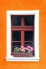 Fototapeta na wymiar Orange paint wall background with window and box full of pink flowers.