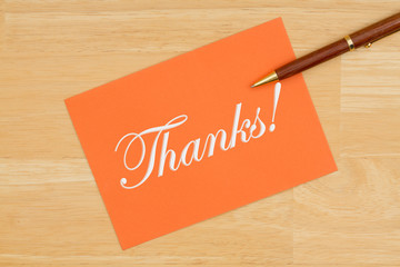 Thanks orange greeting card with a pen on textured wood