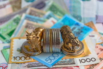 Bronze figures of a bull and a bear near metal coins on the background of paper money. Blur...