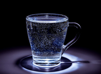 Glass mug with cold water in a dark tonality. Top lighting. Close-up.