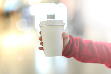The child is holding a cup of drink against the blurry lights of a shopping center
