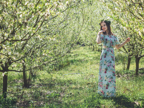 Young beautiful brunette woman in long dress spring blossom trees.