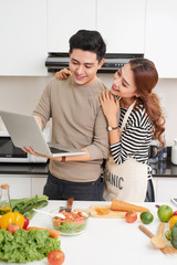 Beautiful young couple is using a digital tablet and smiling while cooking in kitchen at home