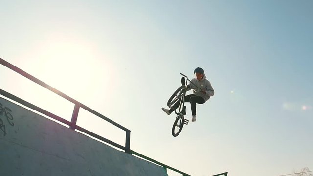 A bmx riders training their skills in the skatepark. Racing up, performing a flip and going down on a bright sun background