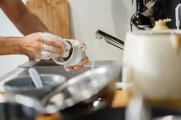 male hand with a sponge to wash the foam cup in the sink in the kitchen with the inclusion of water.