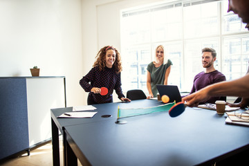 Laughing colleagues playing table tennis together on a boardroom